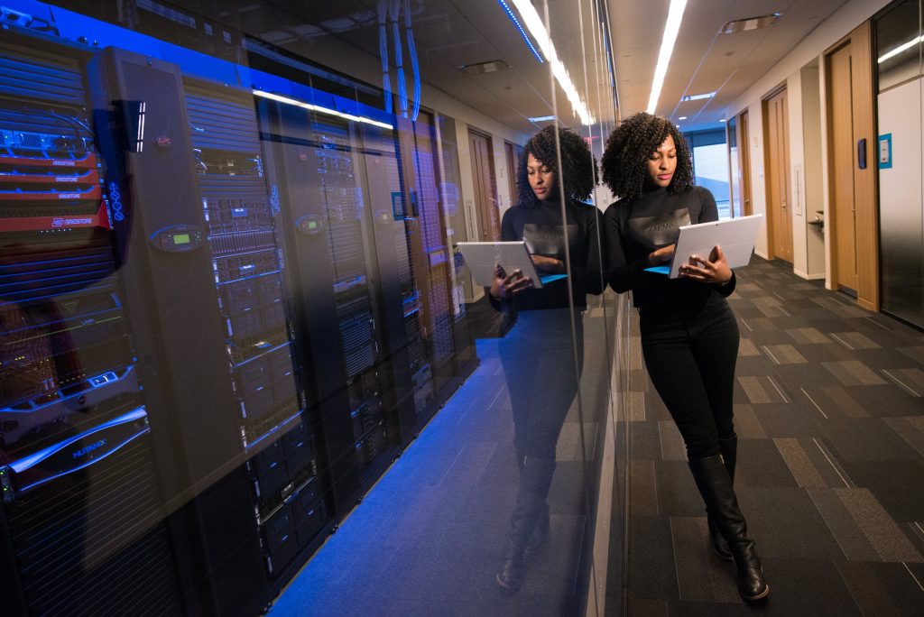 Woman leaning against window of server toom looking at laptop