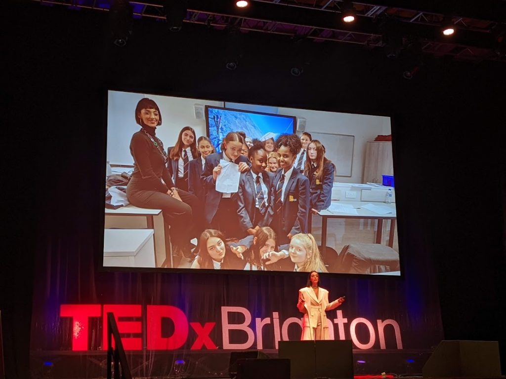 Biana Cefalo on TedX Brighton stage with a photo of girls at school behind her