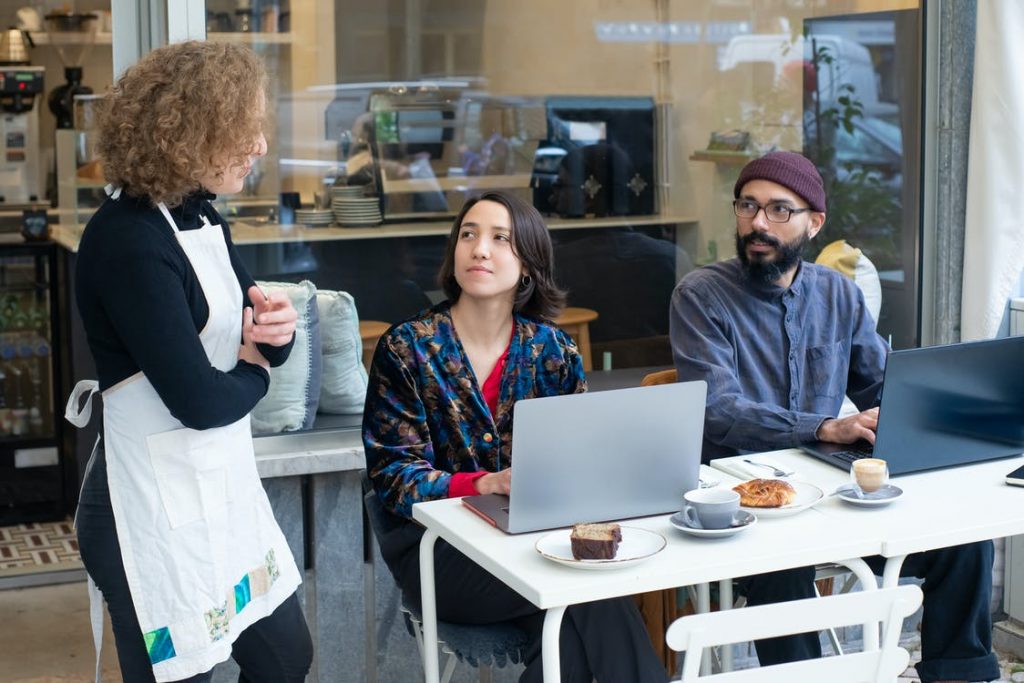 2 people working outside a cafe with laptops, with waitress standing